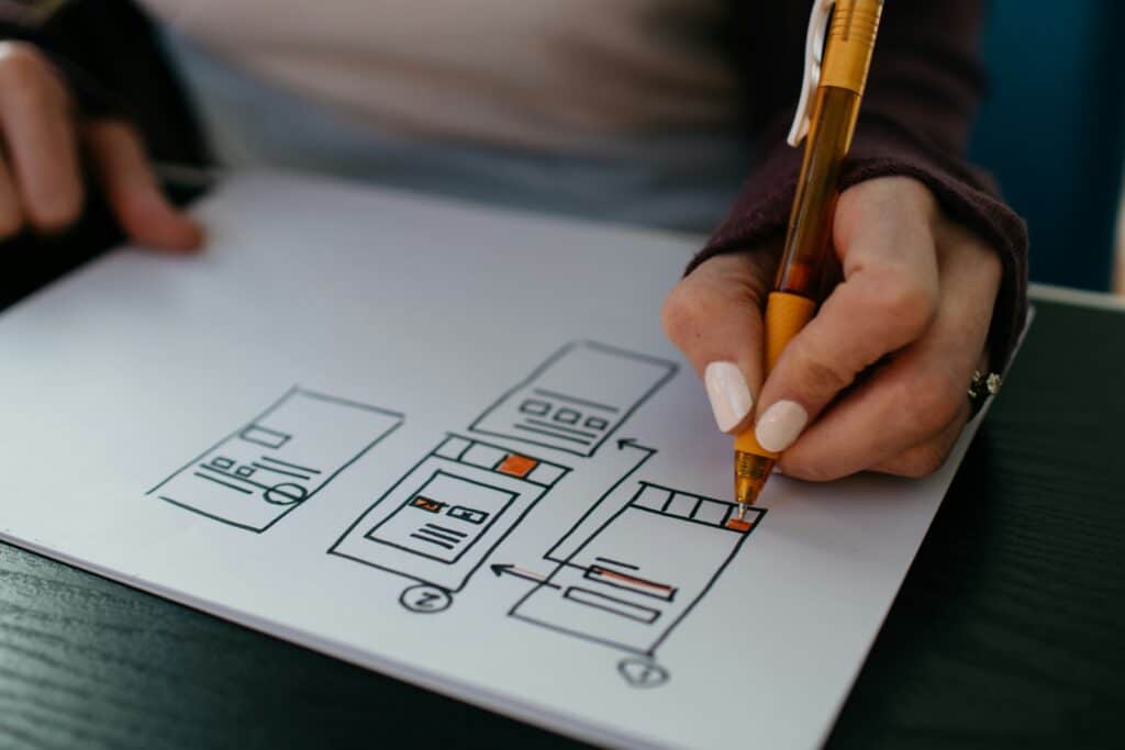 A close up of a hand manually drawing a UX design on paper