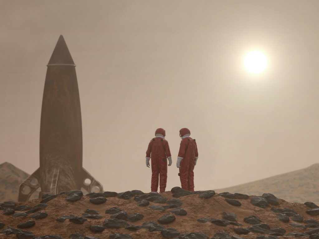 Two astronauts in red suits stand on a rocky, desert-like landscape beside a retro rocket, under a hazy sky with a bright sun.